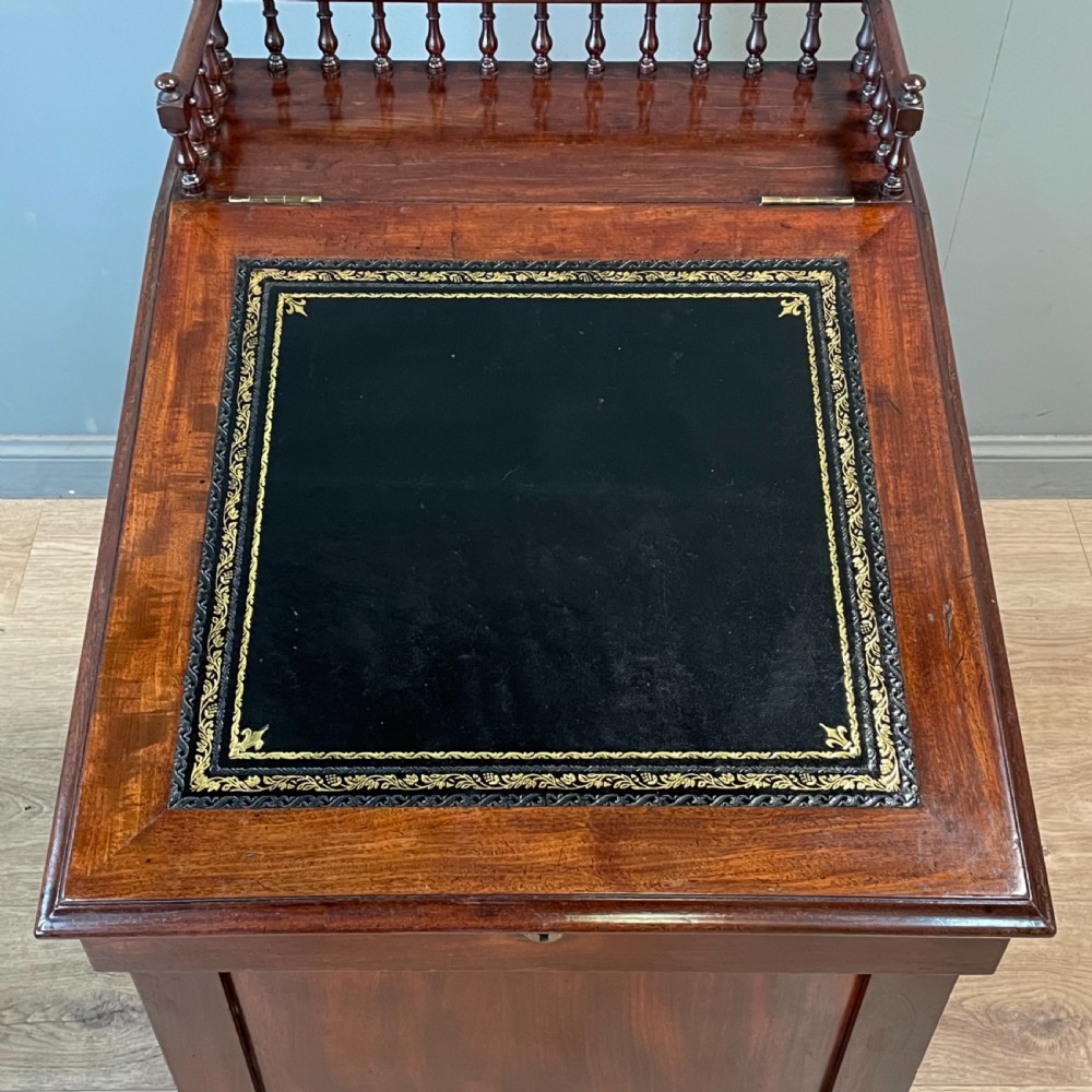 A William IV mahogany Davenport desk featuring a sloped leather writing slope, turned spindle gallery top, side drawers, and brass castors. View VII