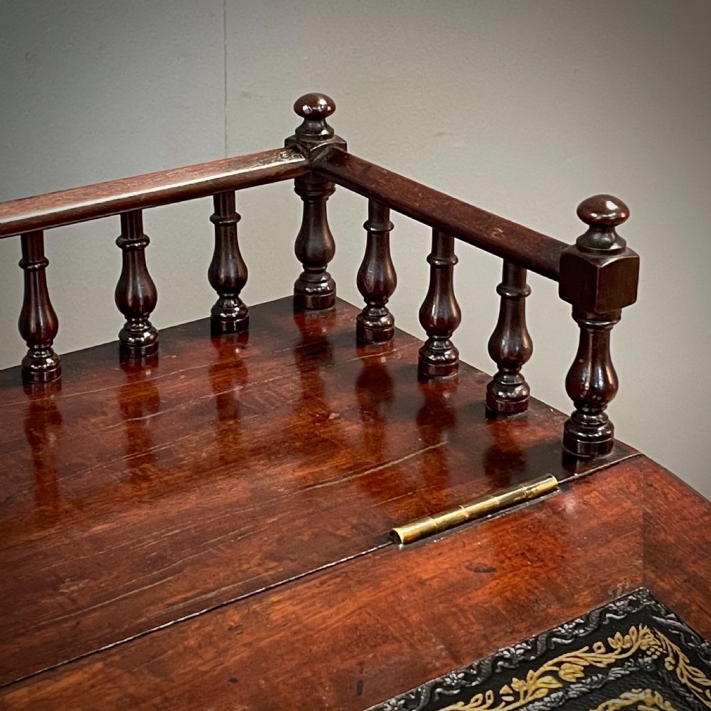 A William IV mahogany Davenport desk featuring a sloped leather writing slope, turned spindle gallery top, side drawers, and brass castors. View IX