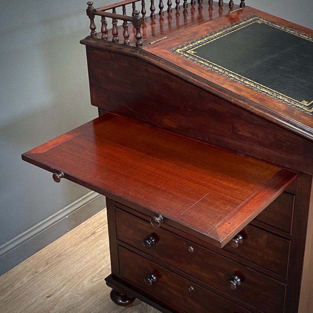 A William IV mahogany Davenport desk featuring a sloped leather writing slope, turned spindle gallery top, side drawers, and brass castors. View X