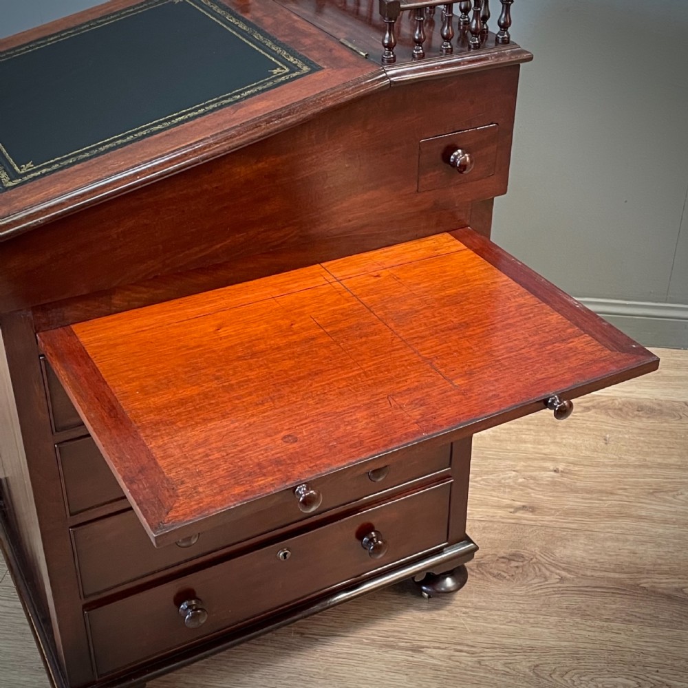 A William IV mahogany Davenport desk featuring a sloped leather writing slope, turned spindle gallery top, side drawers, and brass castors. View XI