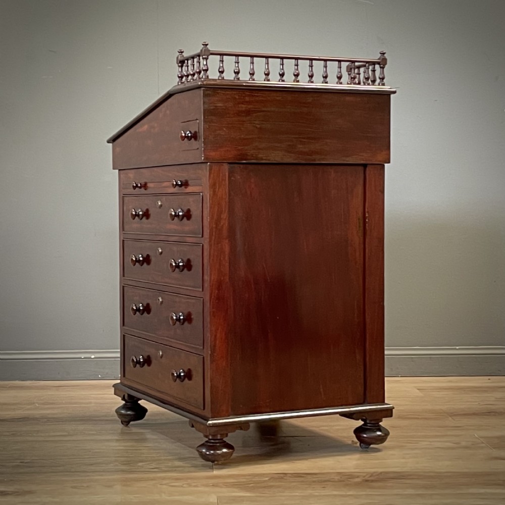 A William IV mahogany Davenport desk featuring a sloped leather writing slope, turned spindle gallery top, side drawers, and brass castors. View XIII