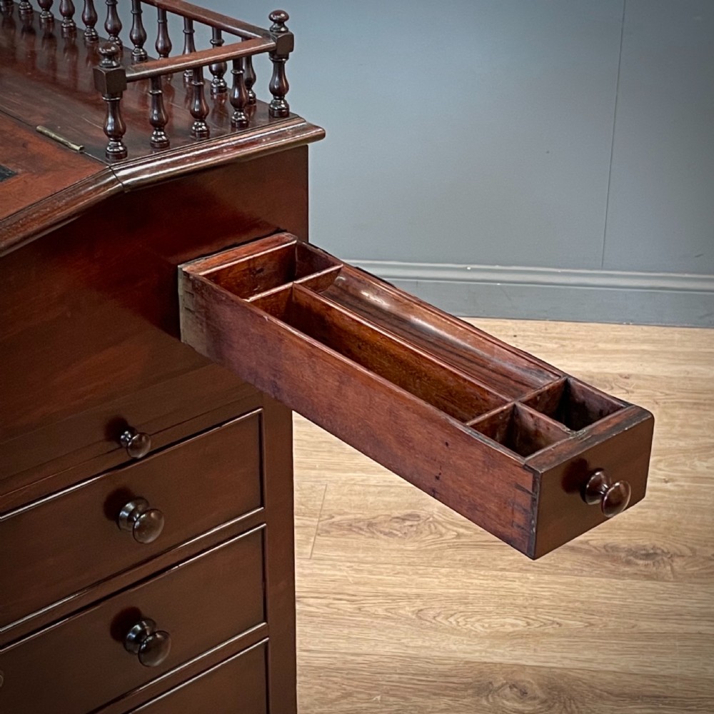 A William IV mahogany Davenport desk featuring a sloped leather writing slope, turned spindle gallery top, side drawers, and brass castors. View XIV