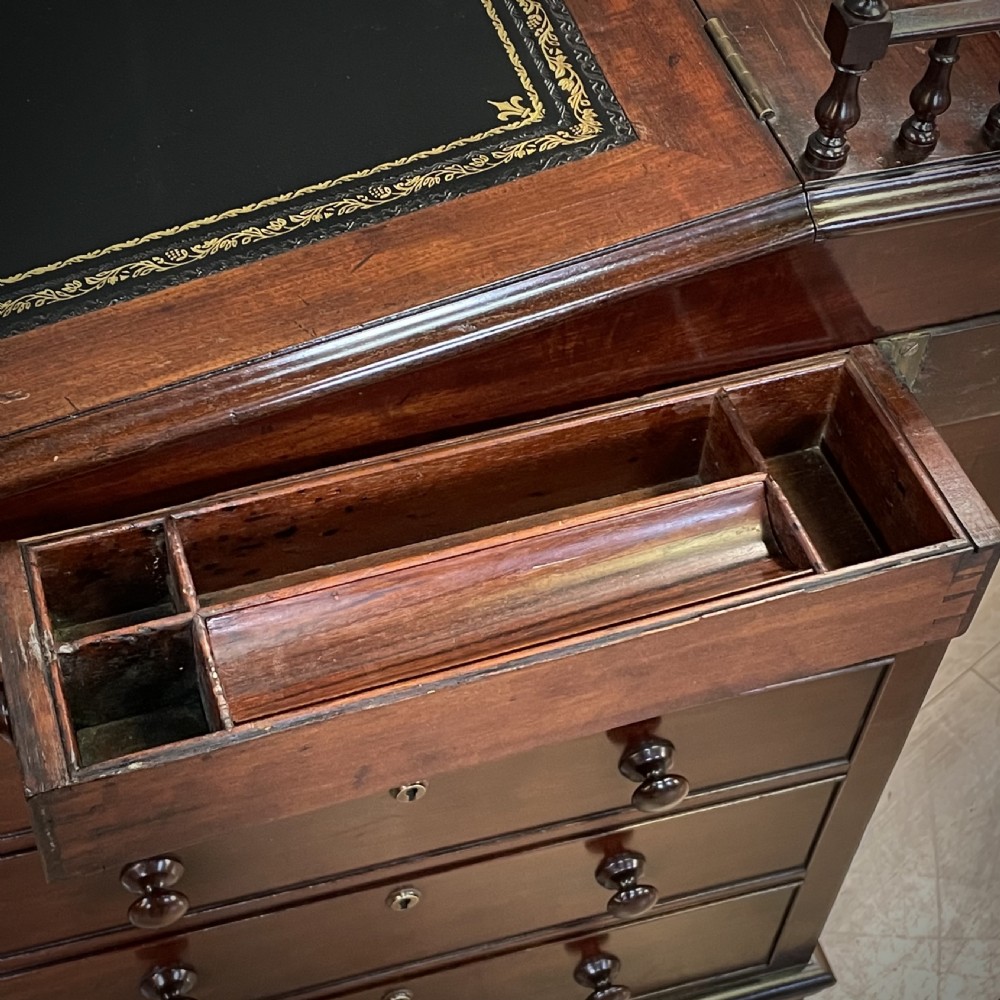 A William IV mahogany Davenport desk featuring a sloped leather writing slope, turned spindle gallery top, side drawers, and brass castors. View XVI