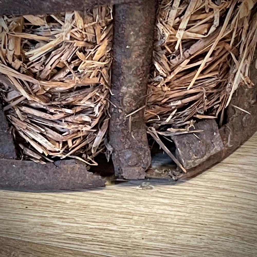 A large green glass demijohn bottle resting inside a natural straw-lined iron basket frame. View VII