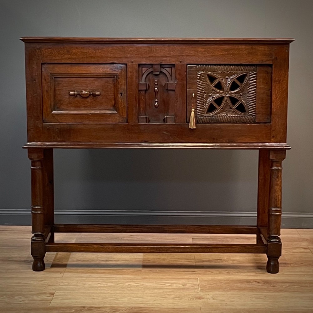 An antique dark oak livery cupboard featuring a carved pierced ventilation panel, central arch motif, turned legs, and a lower stretcher base. View II