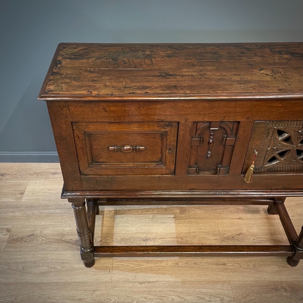 An antique dark oak livery cupboard featuring a carved pierced ventilation panel, central arch motif, turned legs, and a lower stretcher base. View III