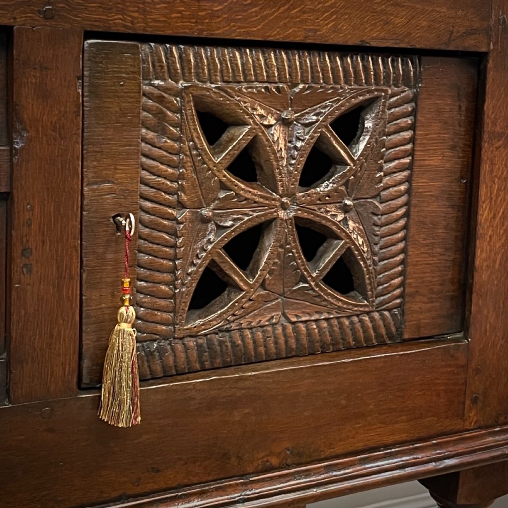 An antique dark oak livery cupboard featuring a carved pierced ventilation panel, central arch motif, turned legs, and a lower stretcher base. View IV