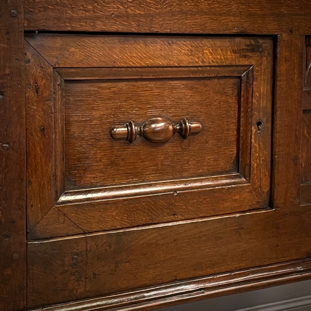 An antique dark oak livery cupboard featuring a carved pierced ventilation panel, central arch motif, turned legs, and a lower stretcher base. View VII