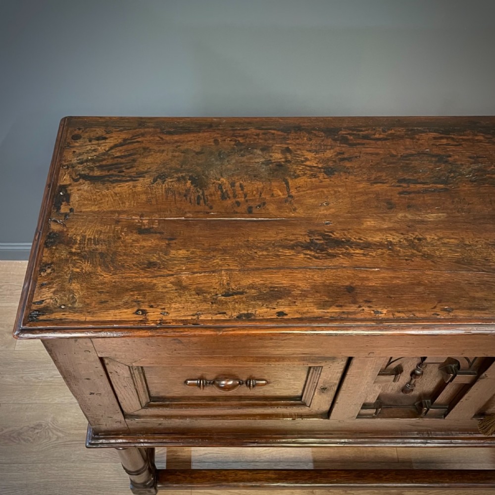 An antique dark oak livery cupboard featuring a carved pierced ventilation panel, central arch motif, turned legs, and a lower stretcher base. View IX