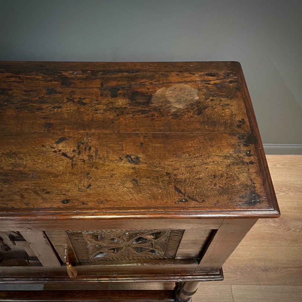 An antique dark oak livery cupboard featuring a carved pierced ventilation panel, central arch motif, turned legs, and a lower stretcher base. View X