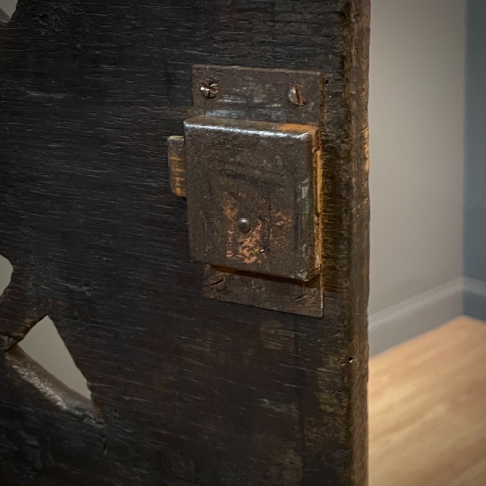 An antique dark oak livery cupboard featuring a carved pierced ventilation panel, central arch motif, turned legs, and a lower stretcher base. View XIV