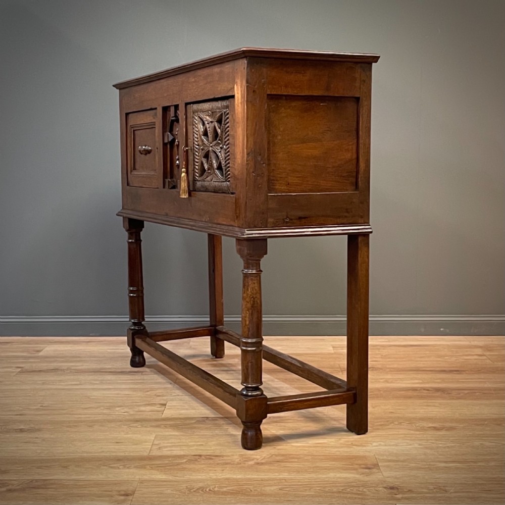 An antique dark oak livery cupboard featuring a carved pierced ventilation panel, central arch motif, turned legs, and a lower stretcher base. View XVII