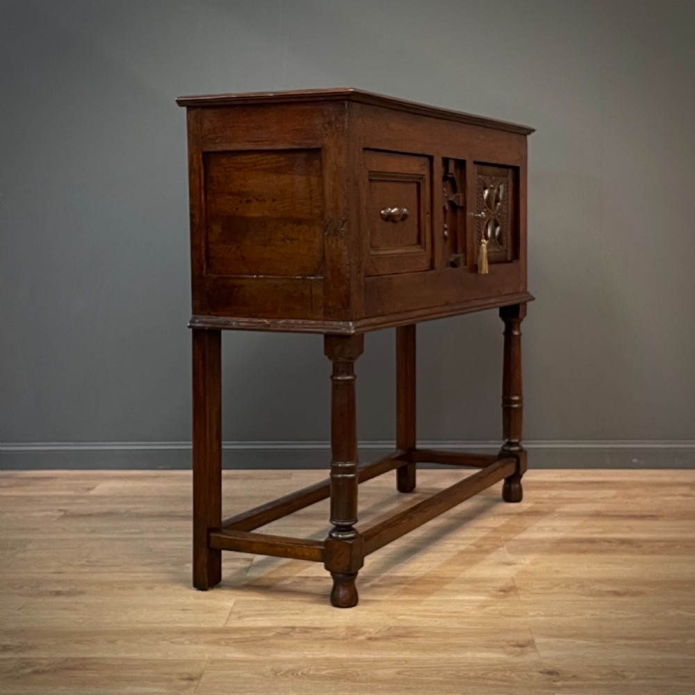 An antique dark oak livery cupboard featuring a carved pierced ventilation panel, central arch motif, turned legs, and a lower stretcher base. View XVIII