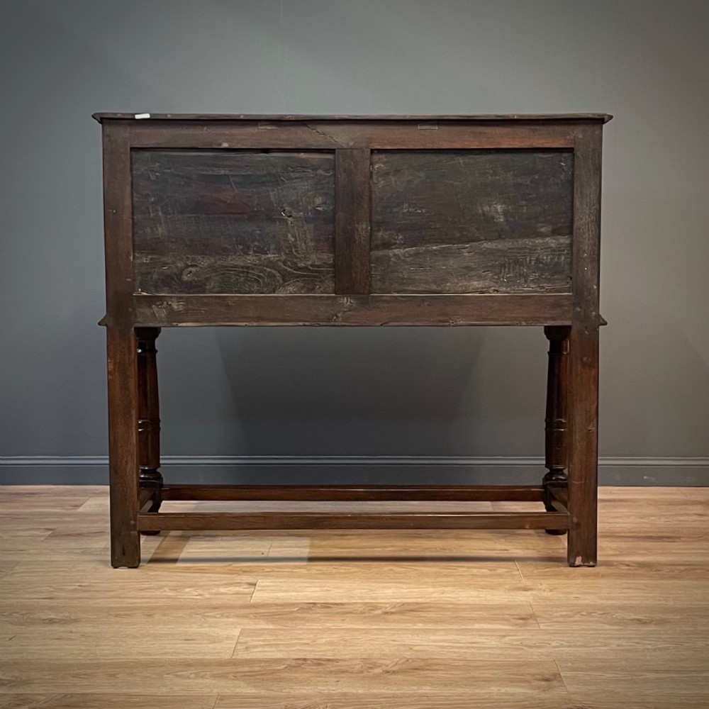 An antique dark oak livery cupboard featuring a carved pierced ventilation panel, central arch motif, turned legs, and a lower stretcher base. View XIX