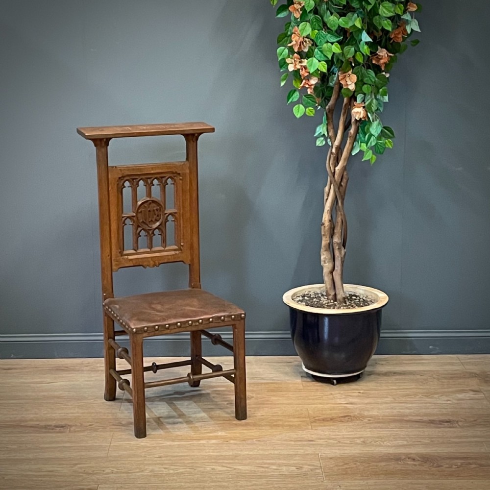 A carved oak Gothic Revival chair featuring a traceried back panel, leather studded seat, and turned stretchers.