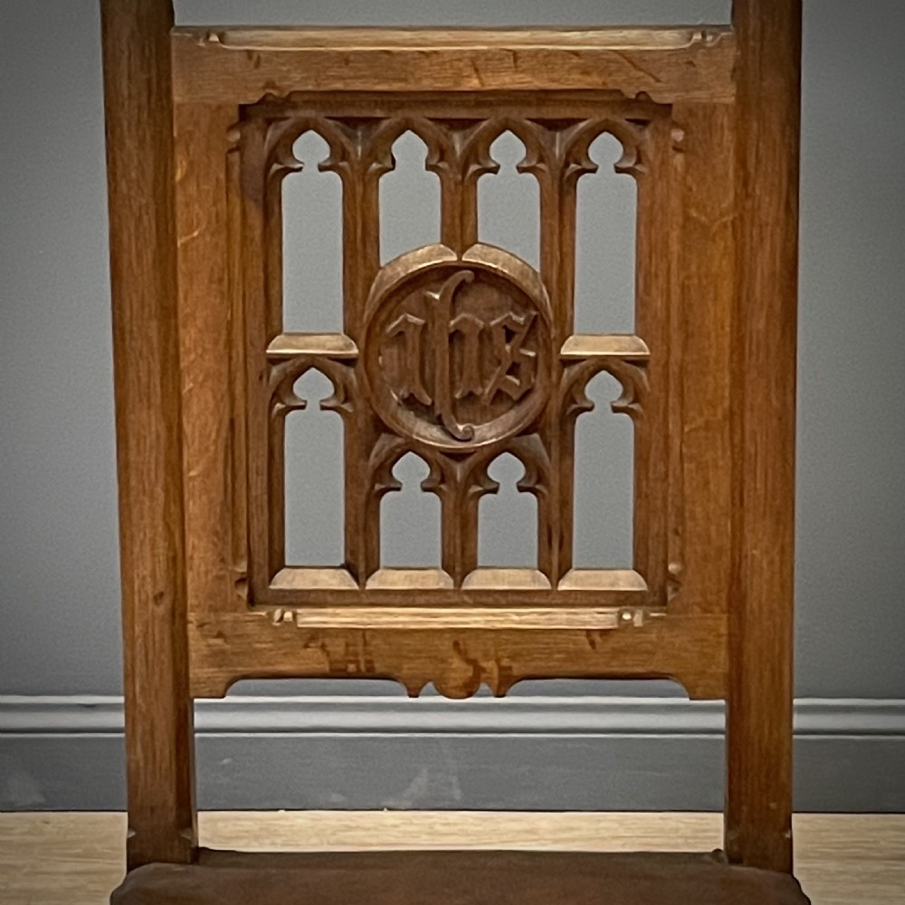 A carved oak Gothic Revival chair featuring a traceried back panel, leather studded seat, and turned stretchers. View V