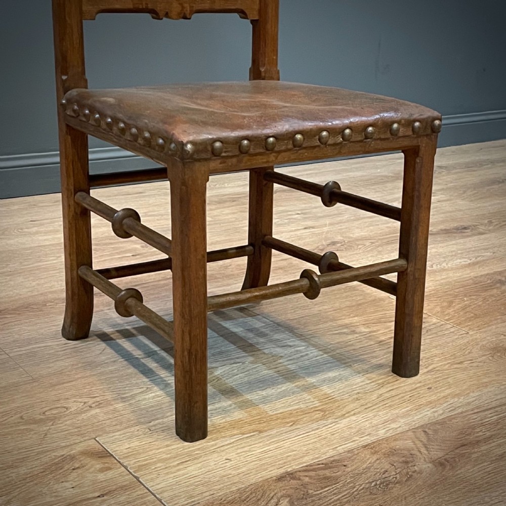 A carved oak Gothic Revival chair featuring a traceried back panel, leather studded seat, and turned stretchers. View VII