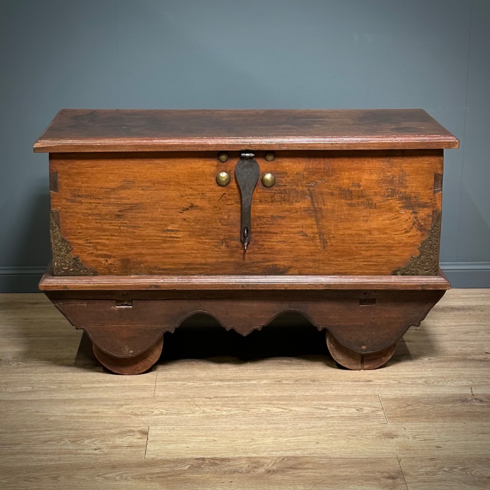 A rustic warm brown teak marriage chest featuring iron latch hardware, brass corner brackets, and a raised wooden base supported by four solid wooden wheels. View II