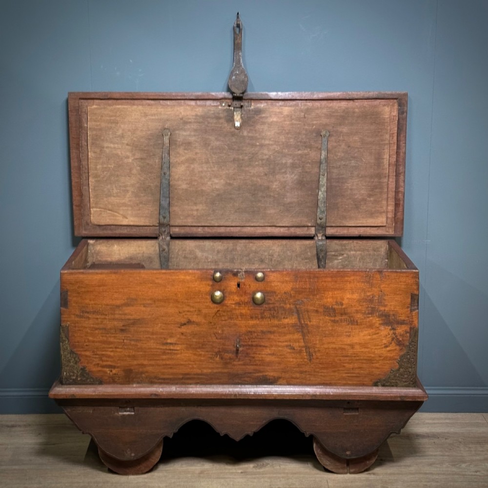A rustic warm brown teak marriage chest featuring iron latch hardware, brass corner brackets, and a raised wooden base supported by four solid wooden wheels. View IV