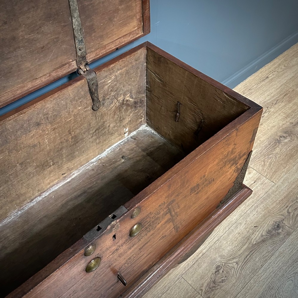 A rustic warm brown teak marriage chest featuring iron latch hardware, brass corner brackets, and a raised wooden base supported by four solid wooden wheels. View VII