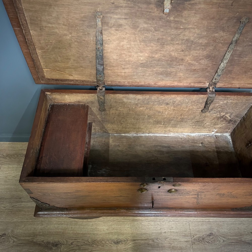 A rustic warm brown teak marriage chest featuring iron latch hardware, brass corner brackets, and a raised wooden base supported by four solid wooden wheels. View VIII