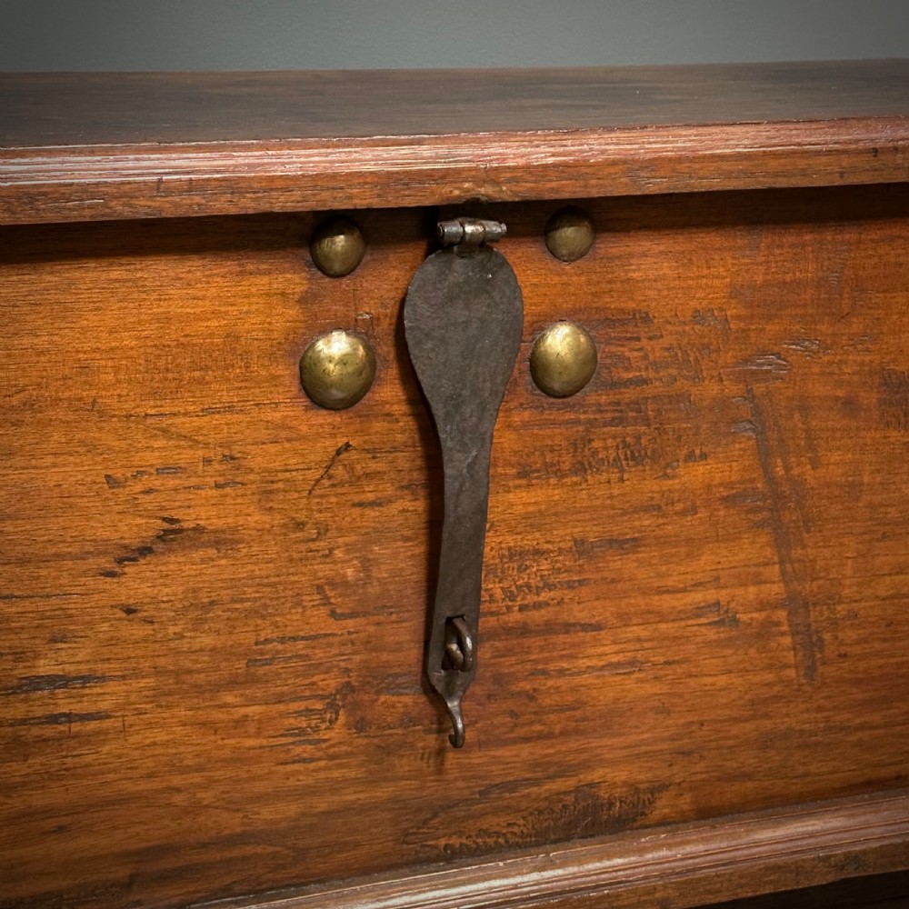 A rustic warm brown teak marriage chest featuring iron latch hardware, brass corner brackets, and a raised wooden base supported by four solid wooden wheels. View XI