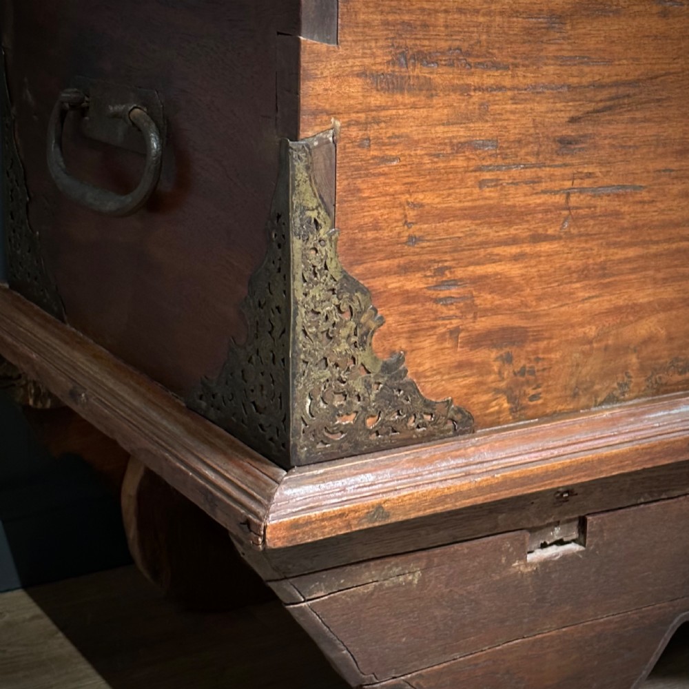 A rustic warm brown teak marriage chest featuring iron latch hardware, brass corner brackets, and a raised wooden base supported by four solid wooden wheels. View XII