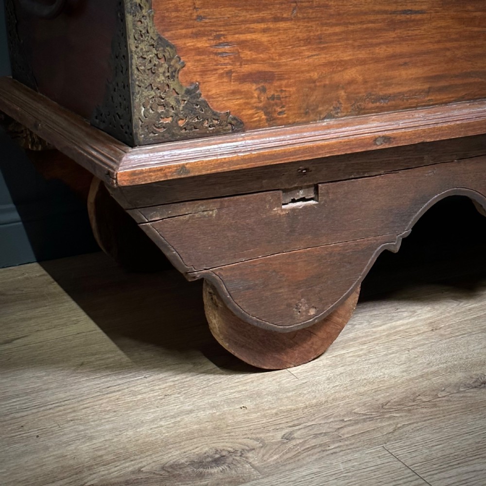 A rustic warm brown teak marriage chest featuring iron latch hardware, brass corner brackets, and a raised wooden base supported by four solid wooden wheels. View XIII