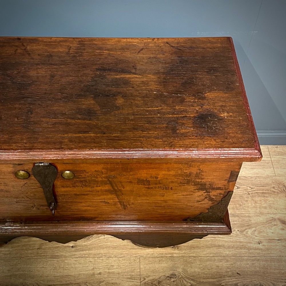 A rustic warm brown teak marriage chest featuring iron latch hardware, brass corner brackets, and a raised wooden base supported by four solid wooden wheels. View XV
