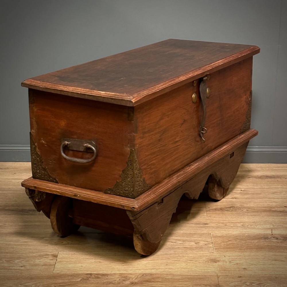 A rustic warm brown teak marriage chest featuring iron latch hardware, brass corner brackets, and a raised wooden base supported by four solid wooden wheels. View XVI
