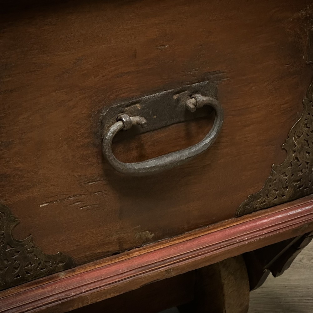 A rustic warm brown teak marriage chest featuring iron latch hardware, brass corner brackets, and a raised wooden base supported by four solid wooden wheels. View XVII