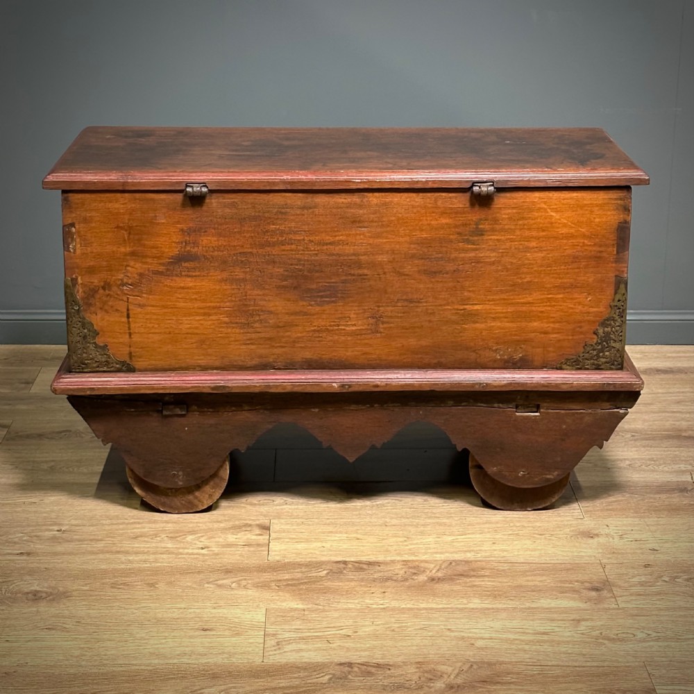 A rustic warm brown teak marriage chest featuring iron latch hardware, brass corner brackets, and a raised wooden base supported by four solid wooden wheels. View XVIII