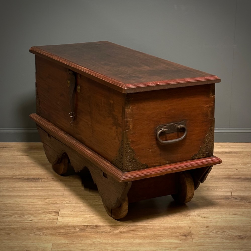 A rustic warm brown teak marriage chest featuring iron latch hardware, brass corner brackets, and a raised wooden base supported by four solid wooden wheels. View XIX