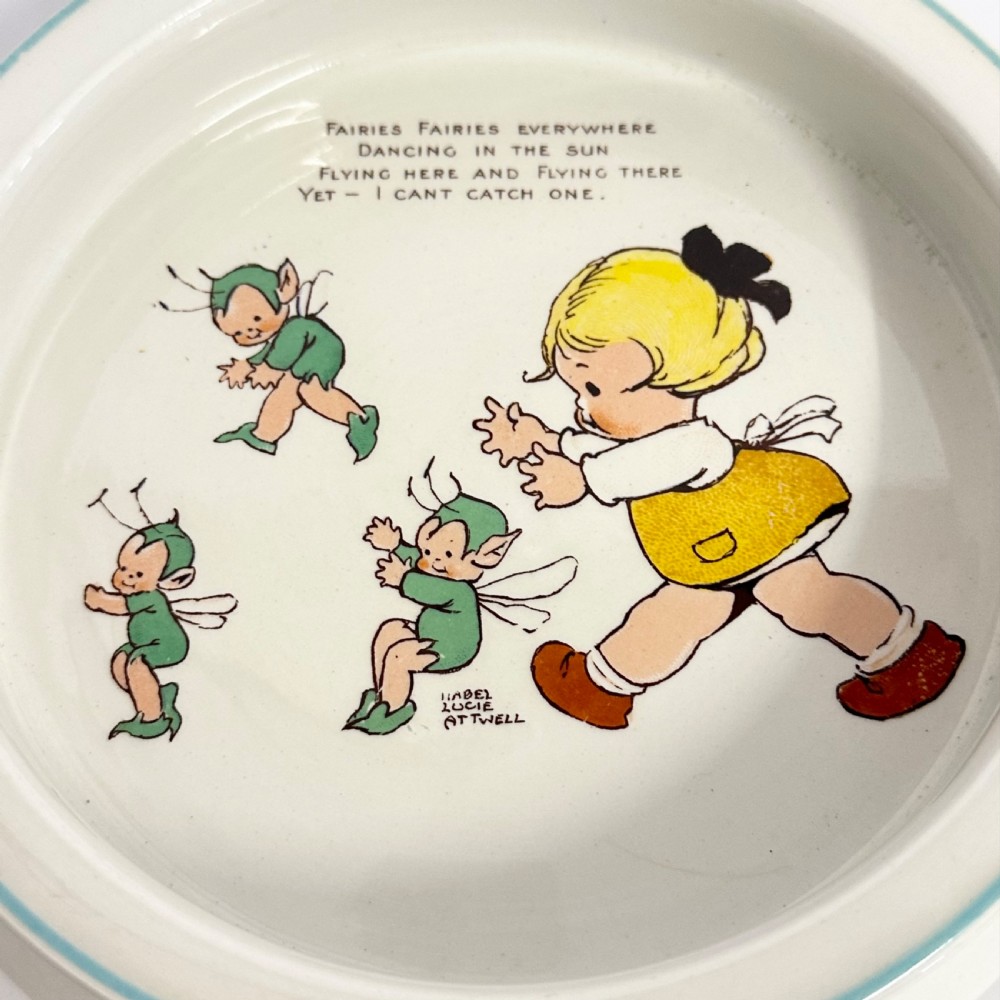 A circular cream glazed ceramic deep baby plate with green rim trim and a central illustration of a child and fairies by Mabel Lucie Attwell. View III