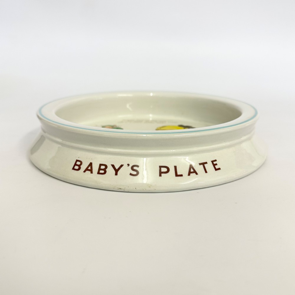 A circular cream glazed ceramic deep baby plate with green rim trim and a central illustration of a child and fairies by Mabel Lucie Attwell. View IV