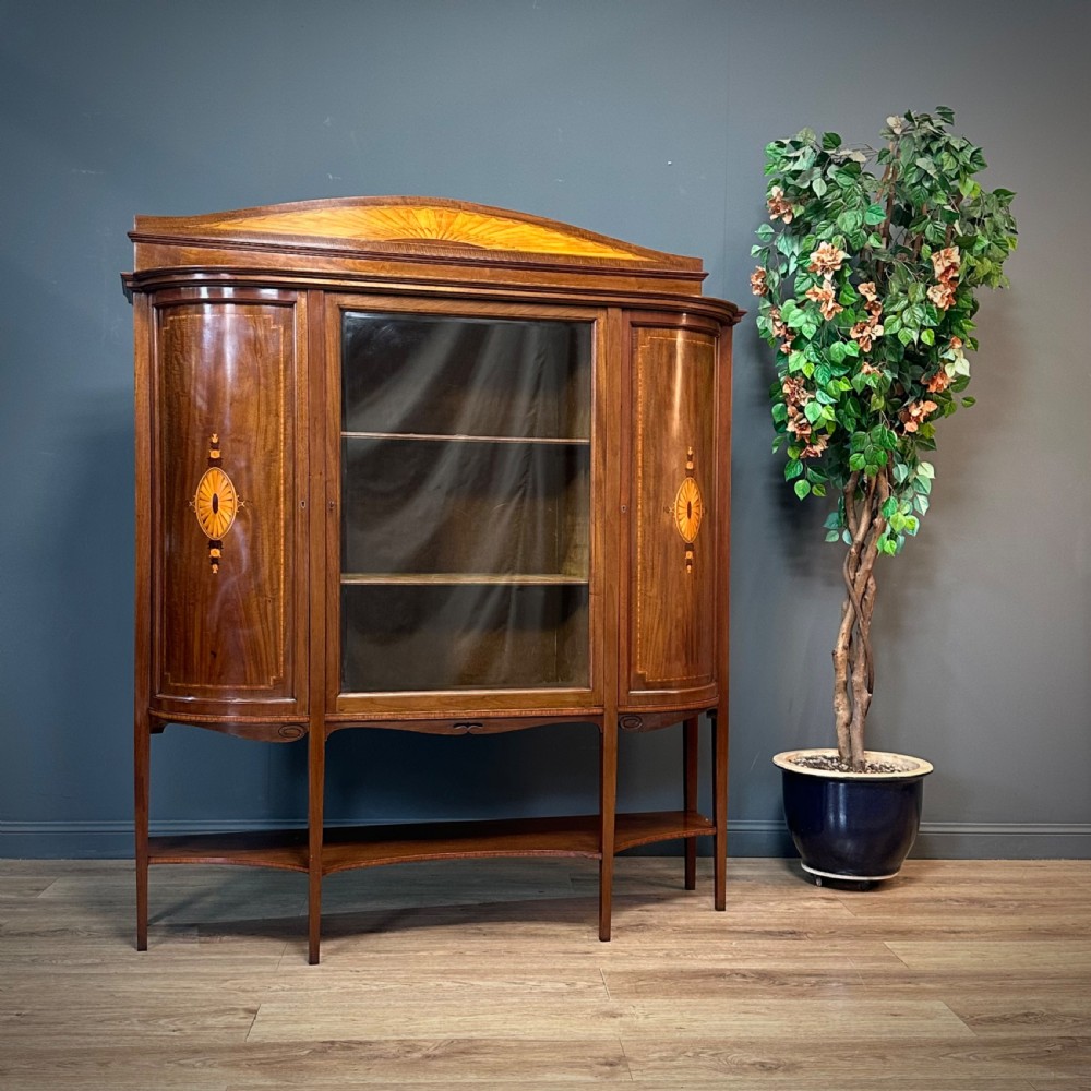 An Edwardian bow-fronted mahogany display cabinet featuring a central glazed door flanked by satinwood oval patera marquetry panels and an arched pediment.