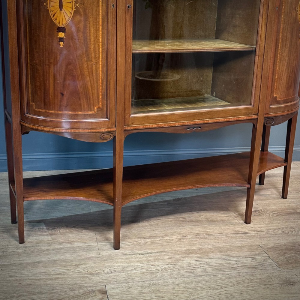 An Edwardian bow-fronted mahogany display cabinet featuring a central glazed door flanked by satinwood oval patera marquetry panels and an arched pediment. View III