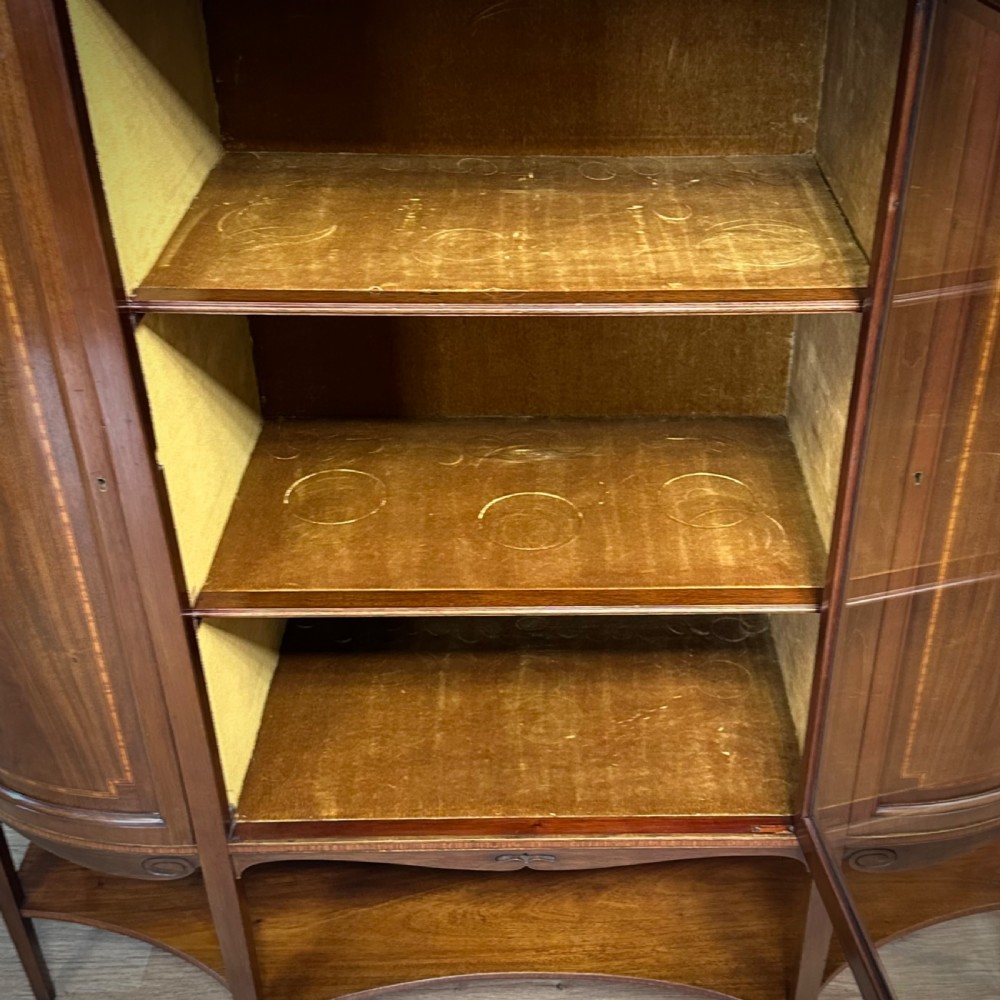 An Edwardian bow-fronted mahogany display cabinet featuring a central glazed door flanked by satinwood oval patera marquetry panels and an arched pediment. View IV