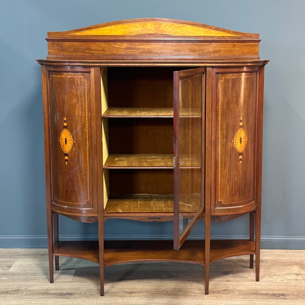 An Edwardian bow-fronted mahogany display cabinet featuring a central glazed door flanked by satinwood oval patera marquetry panels and an arched pediment. View V