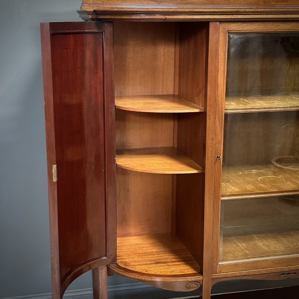 An Edwardian bow-fronted mahogany display cabinet featuring a central glazed door flanked by satinwood oval patera marquetry panels and an arched pediment. View VIII