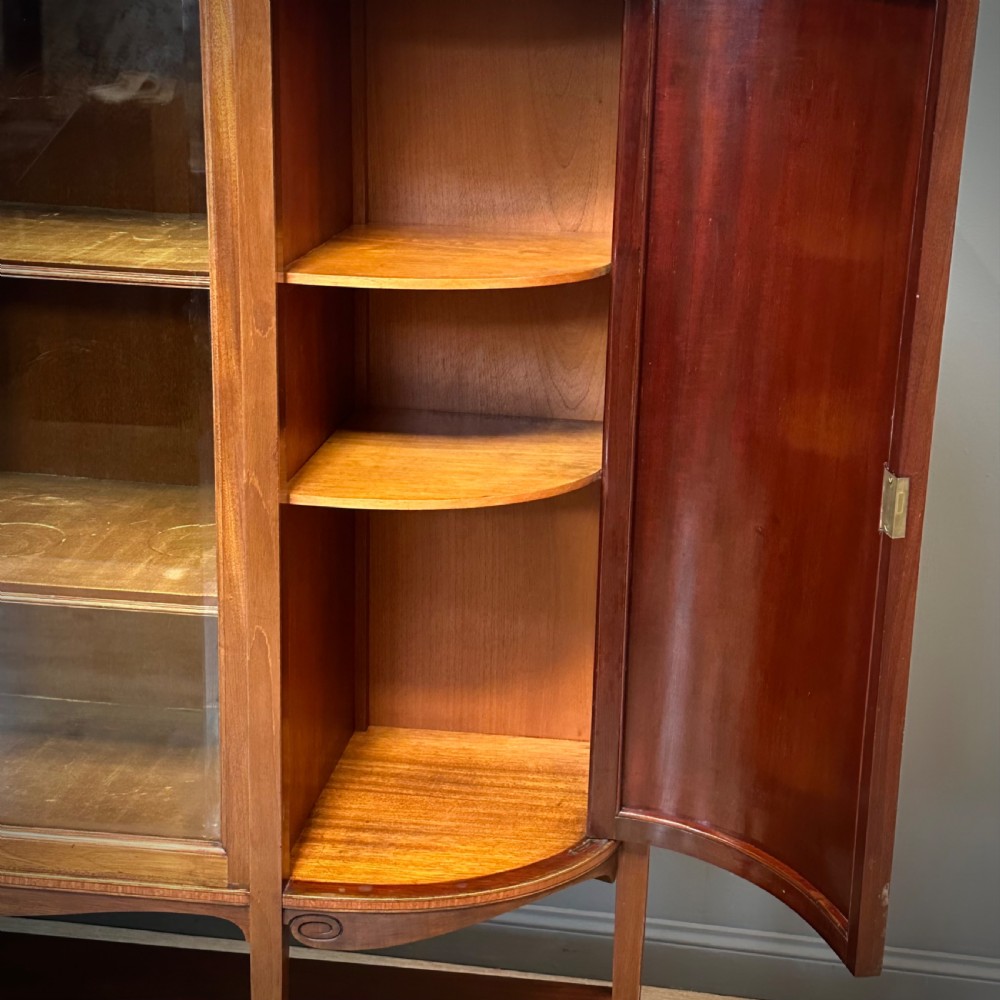 An Edwardian bow-fronted mahogany display cabinet featuring a central glazed door flanked by satinwood oval patera marquetry panels and an arched pediment. View IX