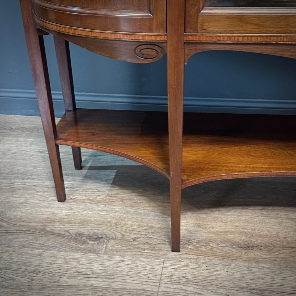 An Edwardian bow-fronted mahogany display cabinet featuring a central glazed door flanked by satinwood oval patera marquetry panels and an arched pediment. View XII