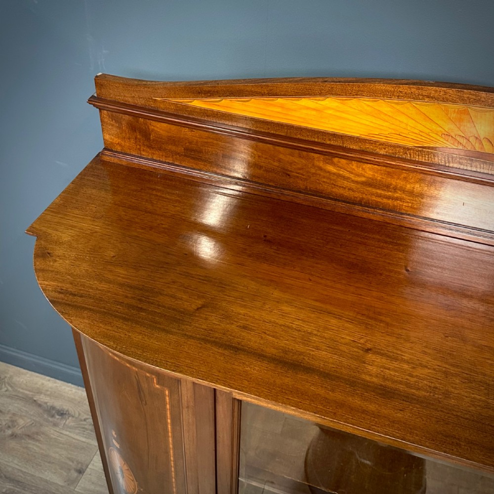 An Edwardian bow-fronted mahogany display cabinet featuring a central glazed door flanked by satinwood oval patera marquetry panels and an arched pediment. View XIII