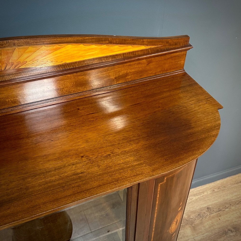 An Edwardian bow-fronted mahogany display cabinet featuring a central glazed door flanked by satinwood oval patera marquetry panels and an arched pediment. View XIV