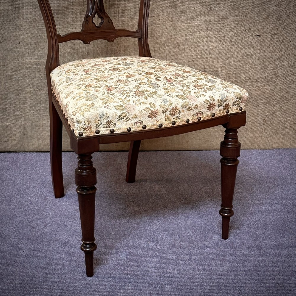 A set of four Edwardian mahogany dining chairs featuring pierced carved splats, patterned floral upholstered seats, and turned front legs. View IV