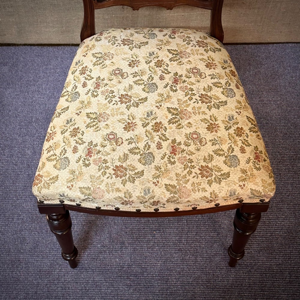 A set of four Edwardian mahogany dining chairs featuring pierced carved splats, patterned floral upholstered seats, and turned front legs. View VI