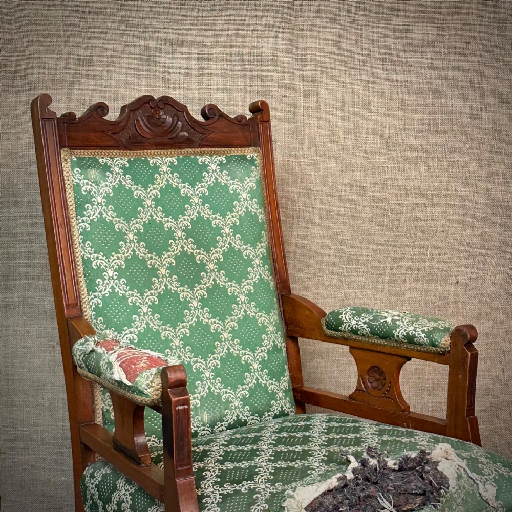 A Victorian carved mahogany armchair featuring a floral cresting rail, turned front legs on castors, and worn green patterned upholstery. View II