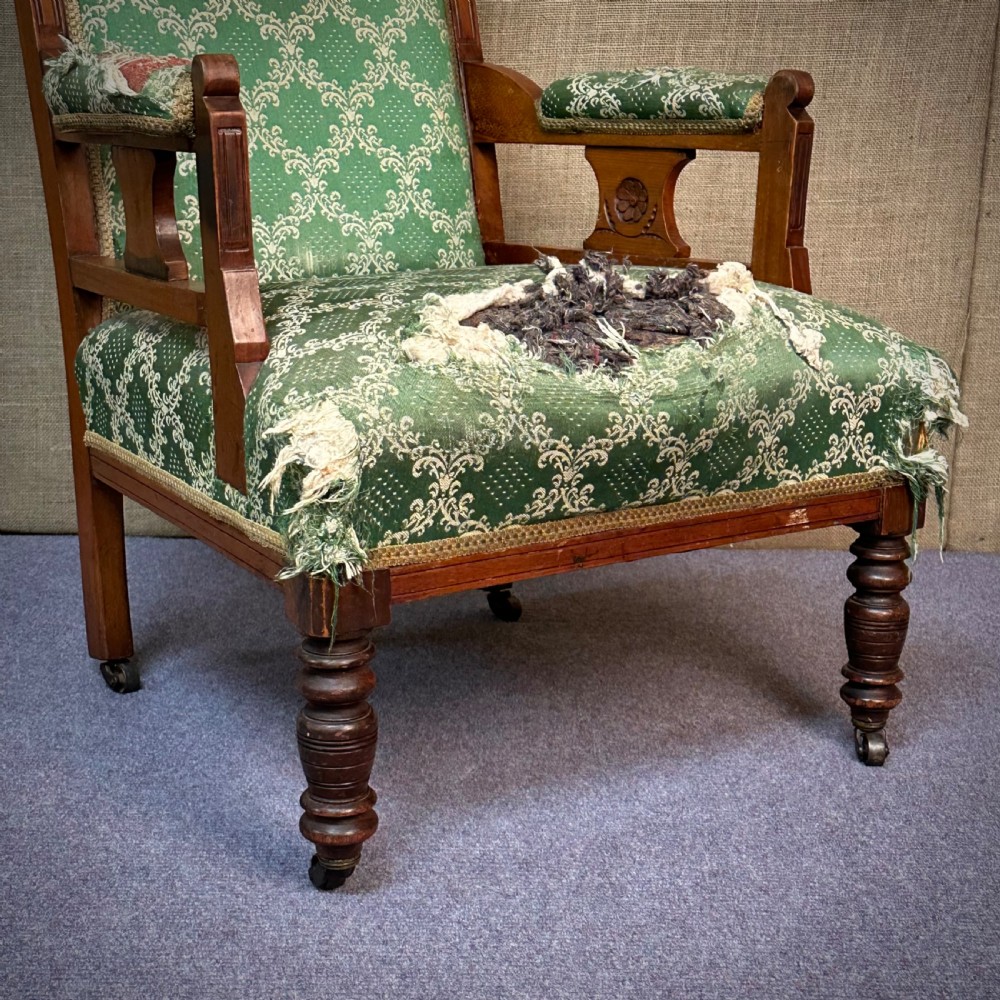 A Victorian carved mahogany armchair featuring a floral cresting rail, turned front legs on castors, and worn green patterned upholstery. View III