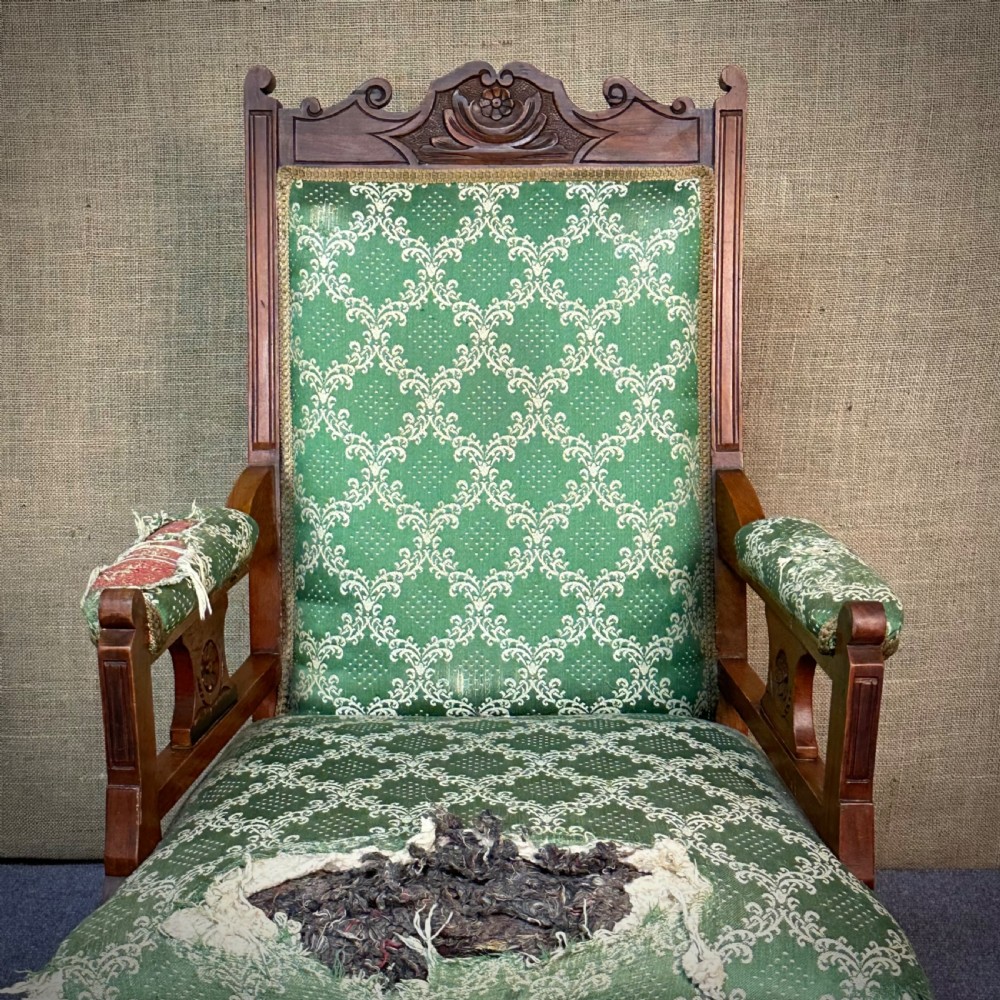 A Victorian carved mahogany armchair featuring a floral cresting rail, turned front legs on castors, and worn green patterned upholstery. View IV