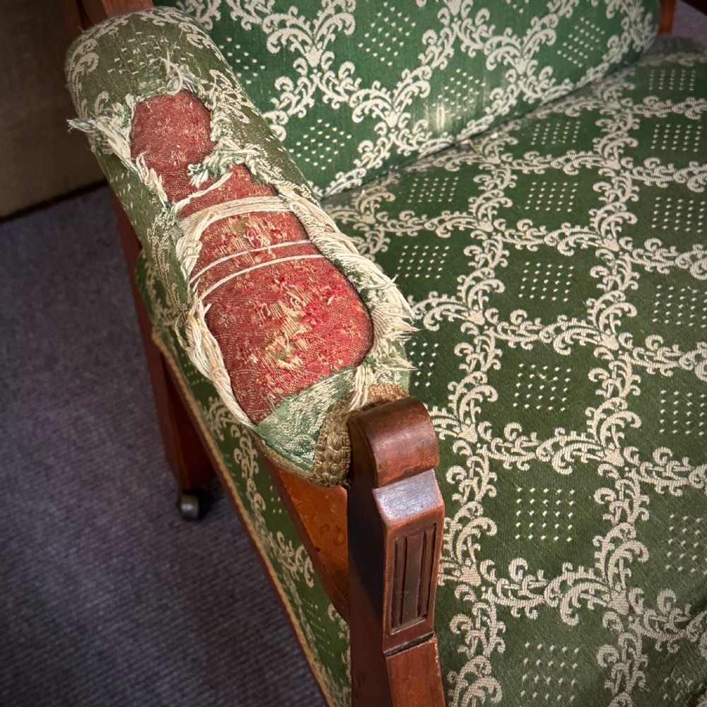 A Victorian carved mahogany armchair featuring a floral cresting rail, turned front legs on castors, and worn green patterned upholstery. View V